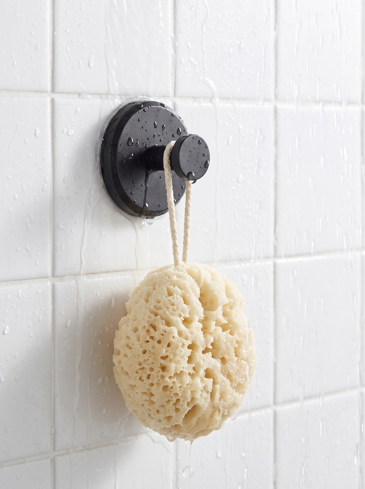 Suction cup hook on a white tiled shower wall holding a sponge